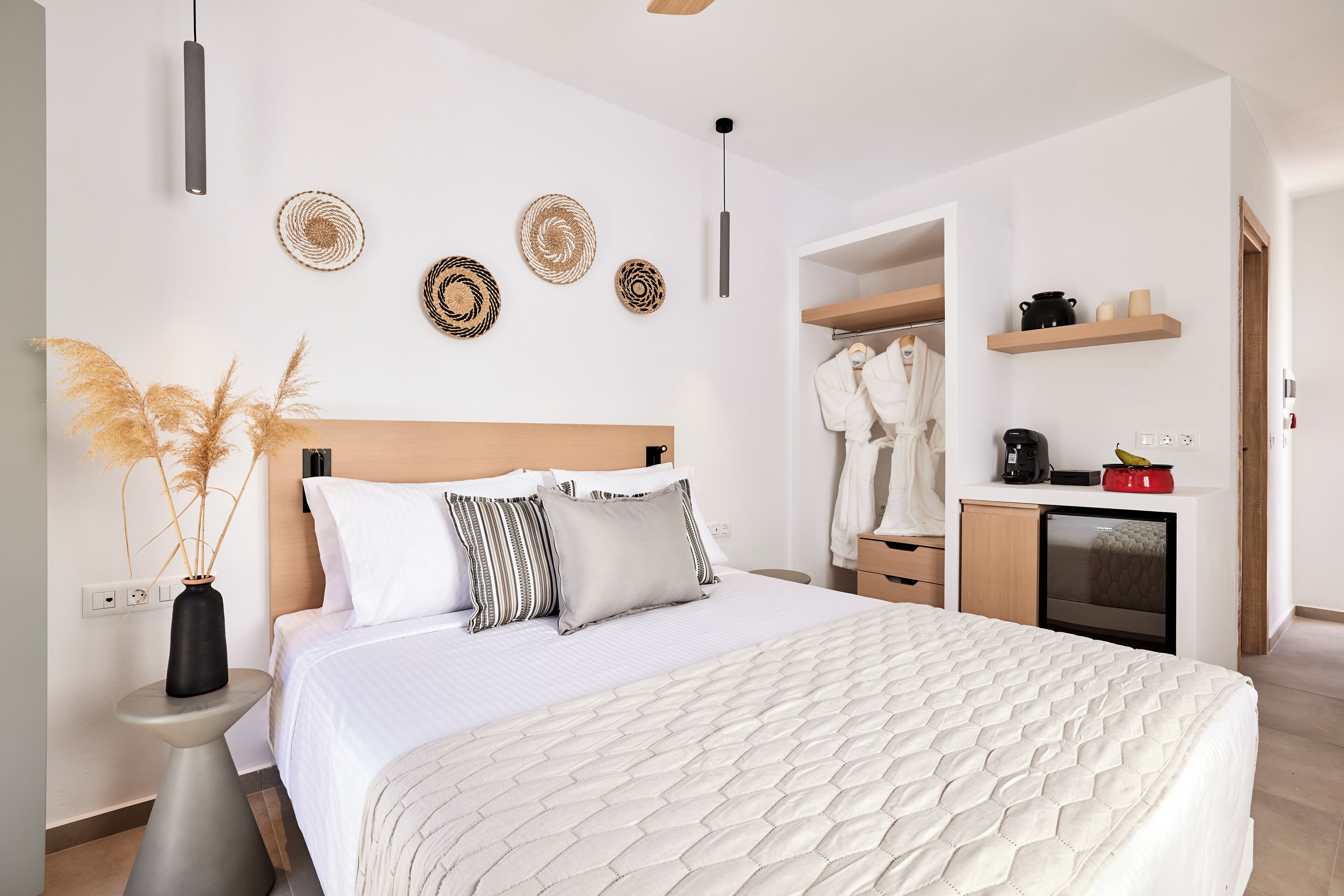 A modern bedroom with a large bed, bedside tables, a wardrobe, and a small kitchenette.