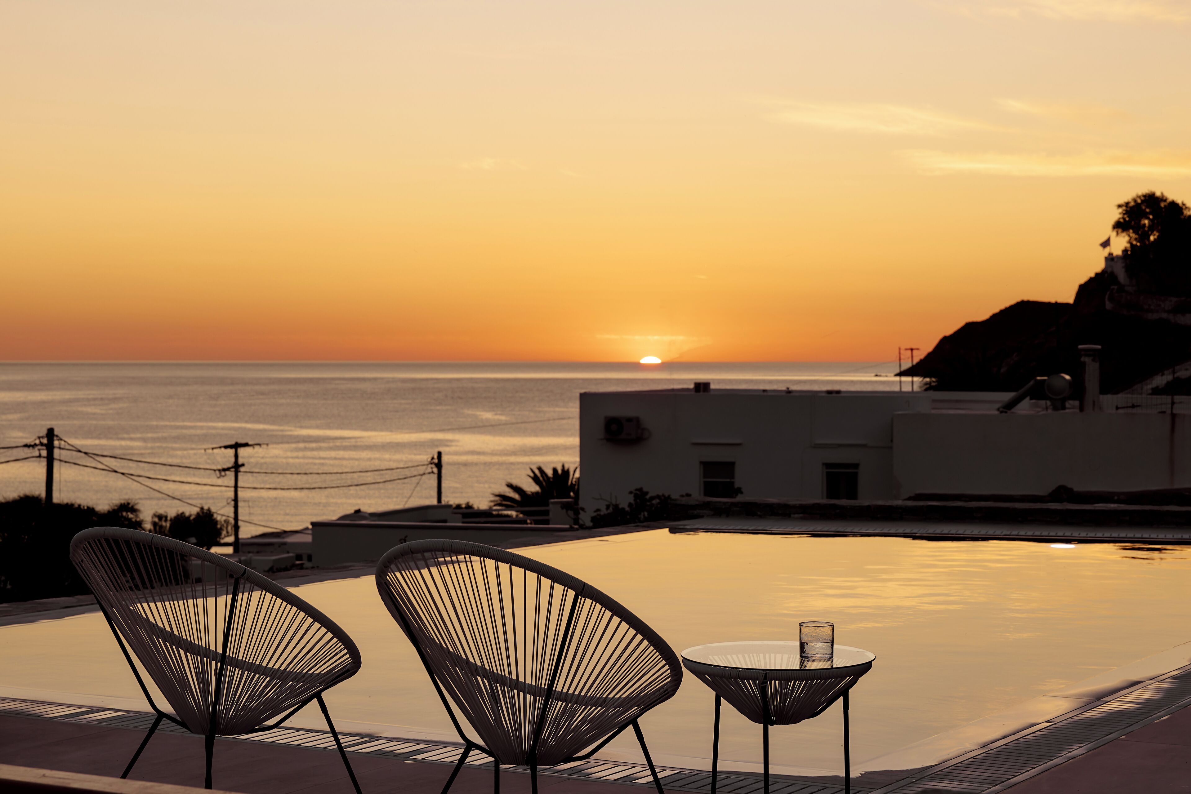 A sunset view from a poolside area with two chairs and a table.