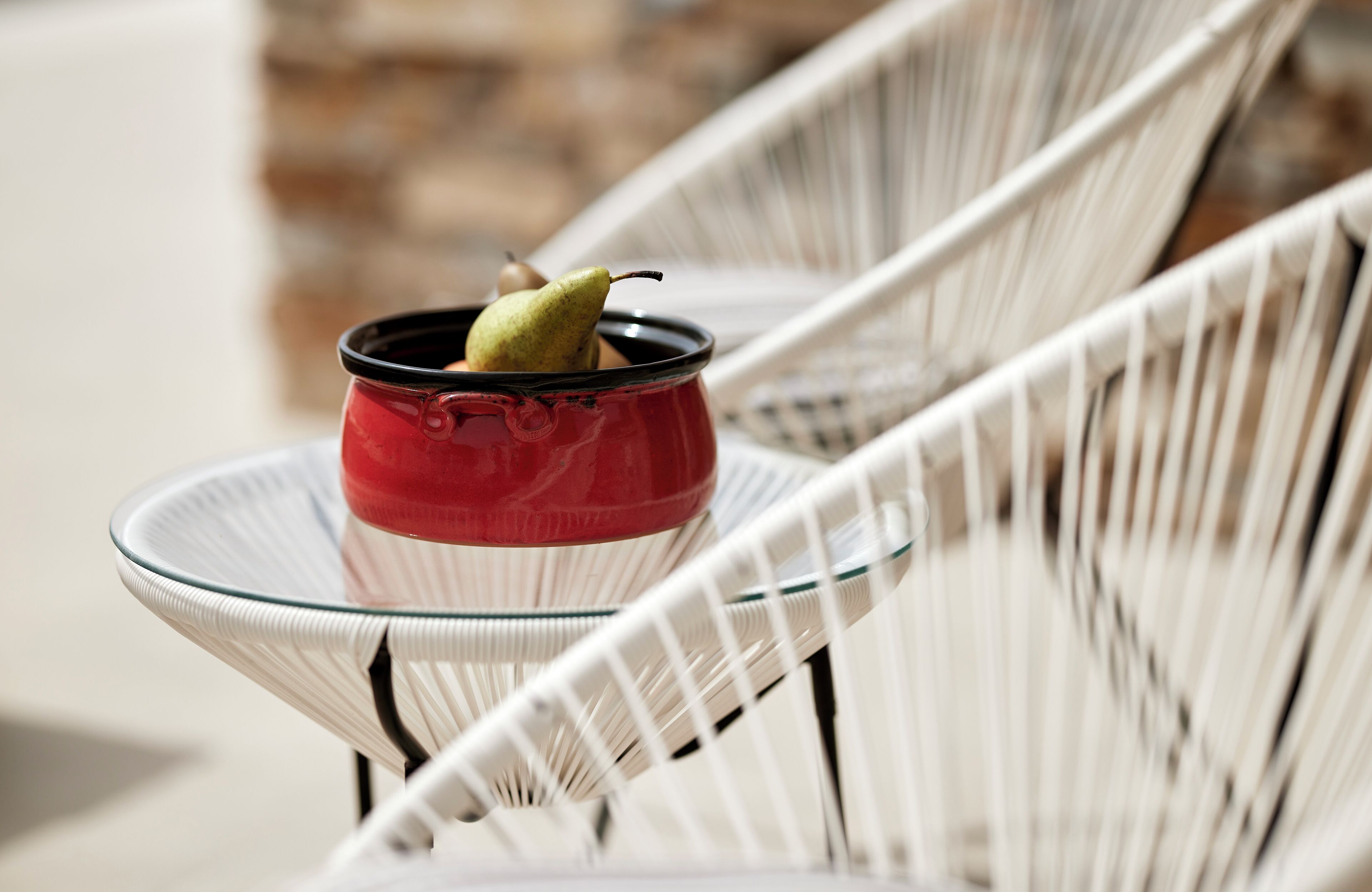 A red bowl with a pear on a glass table.