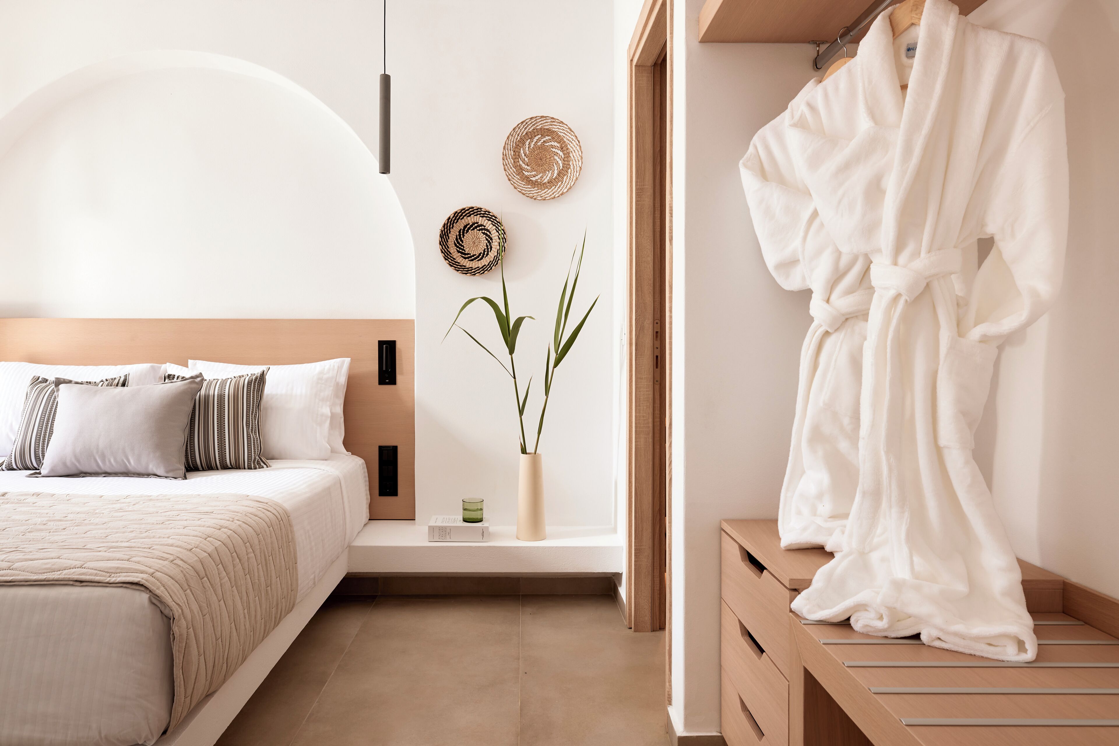 Un dormitorio con cama, mesita de noche y bata colgada en un perchero de madera.