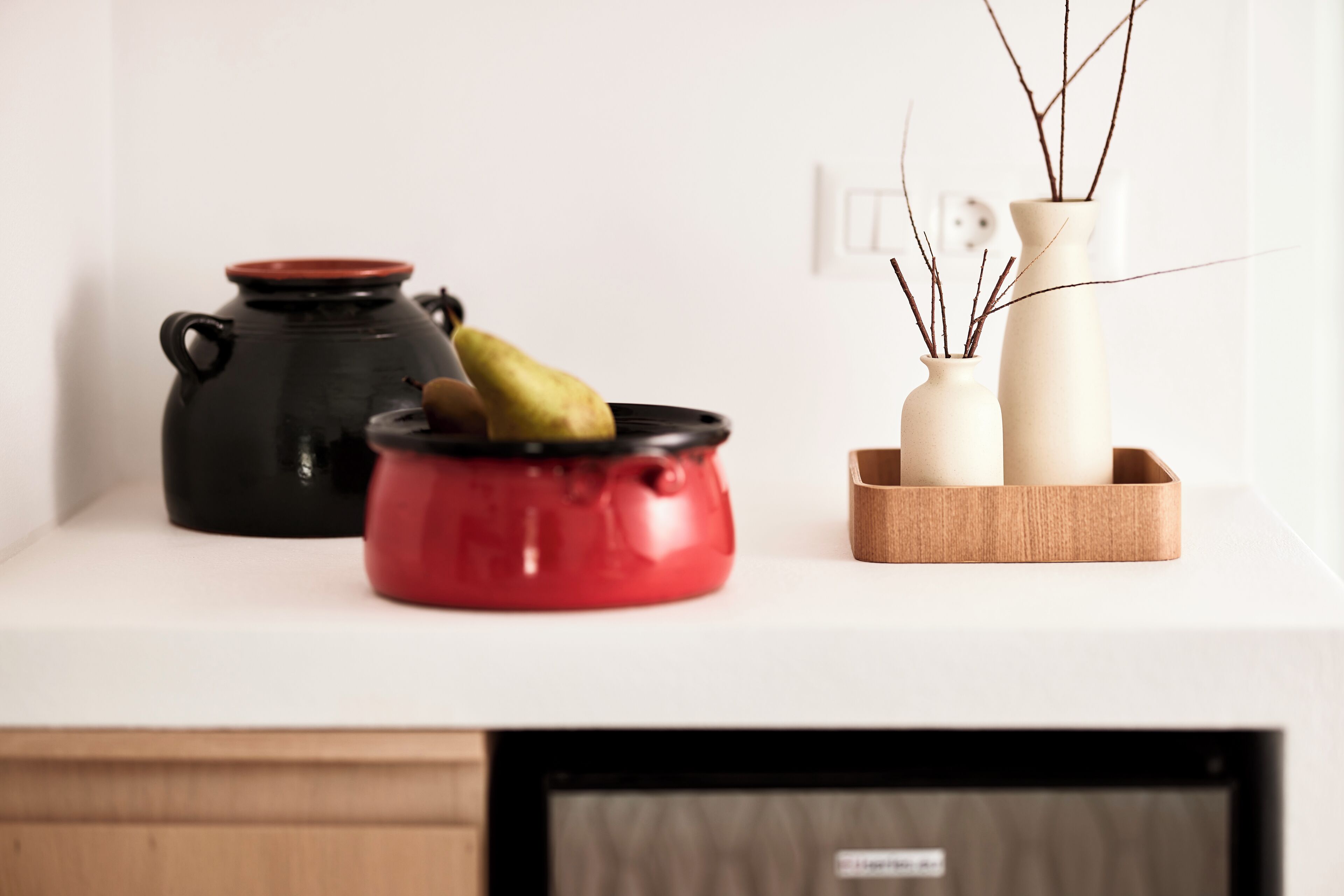 A kitchen counter with two pots, one red and one black, and two white vases with branches.