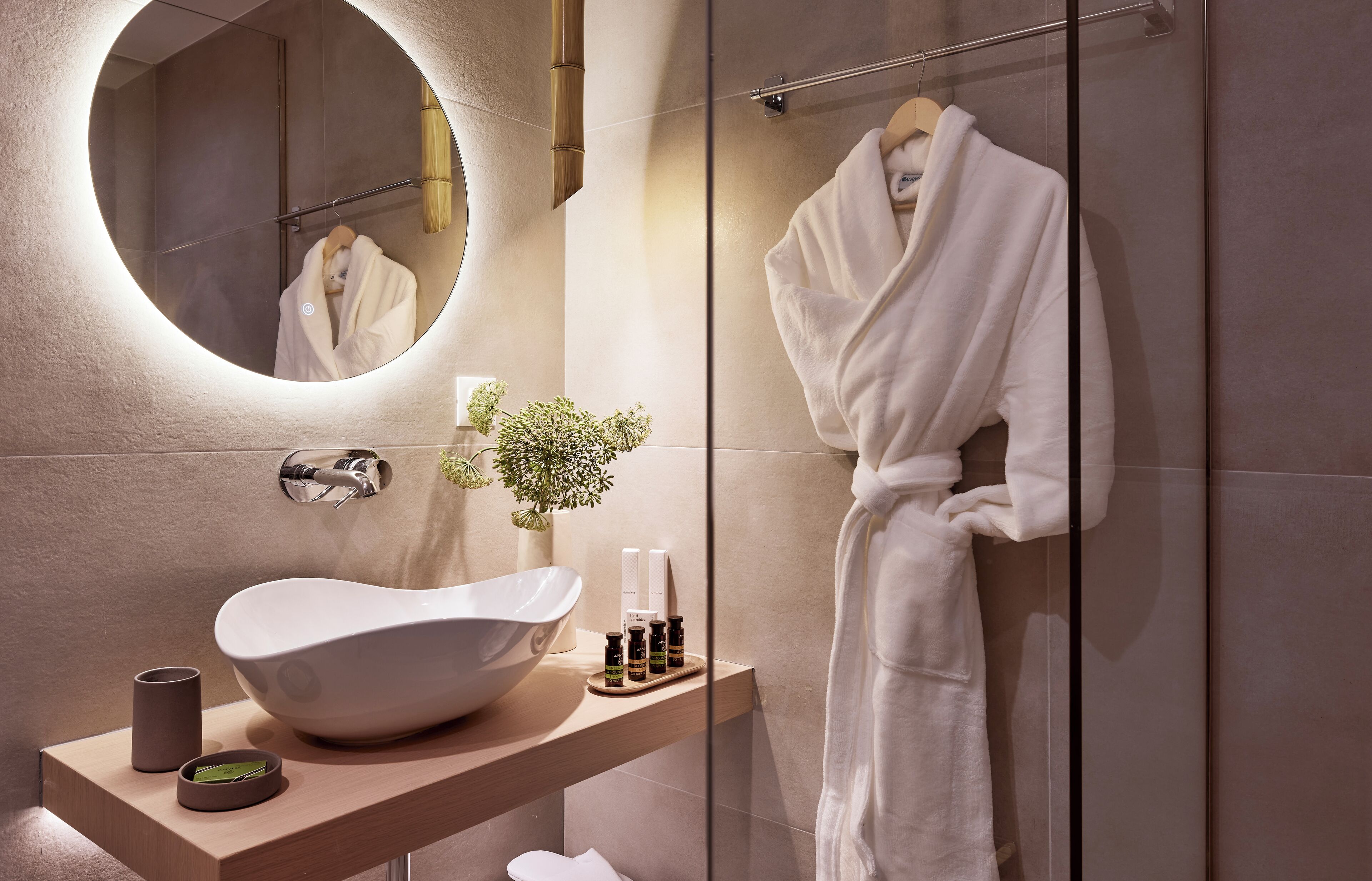 A modern bathroom with a round mirror, a white sink, and a robe hanging on a rack.