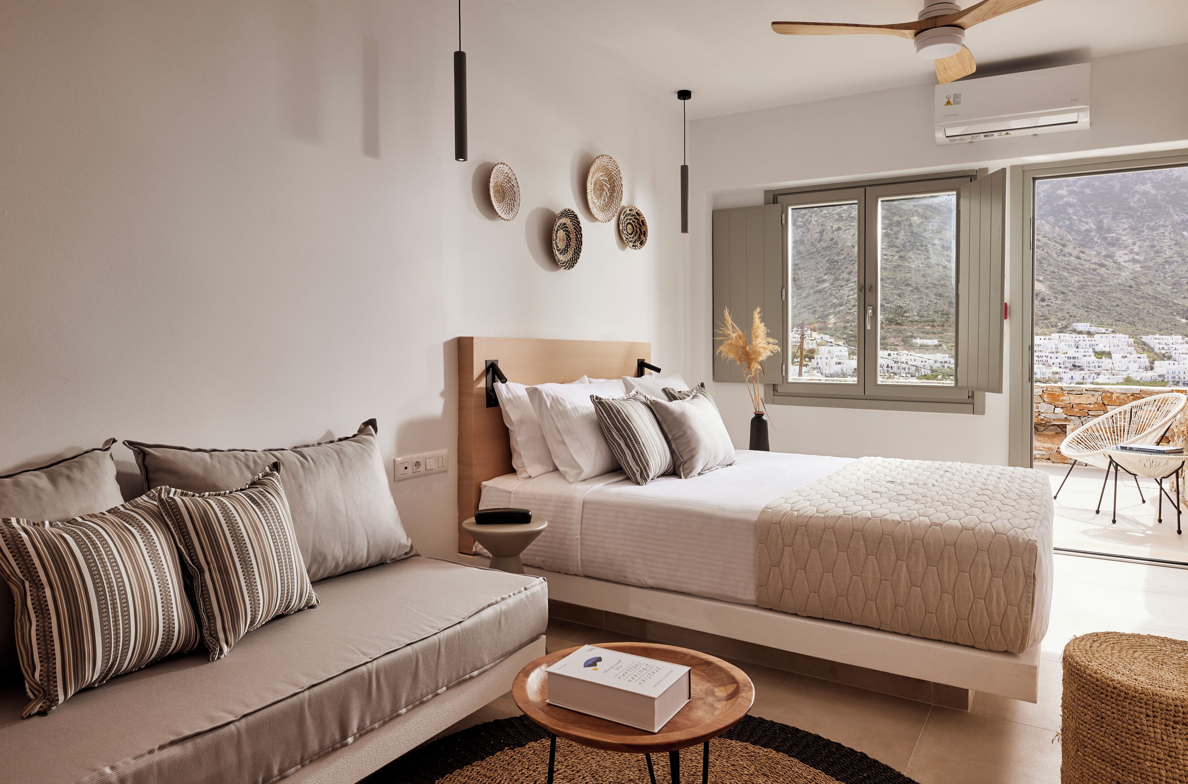A modern bedroom with a large bed, a sofa, and a view of a mountainous landscape through the window.