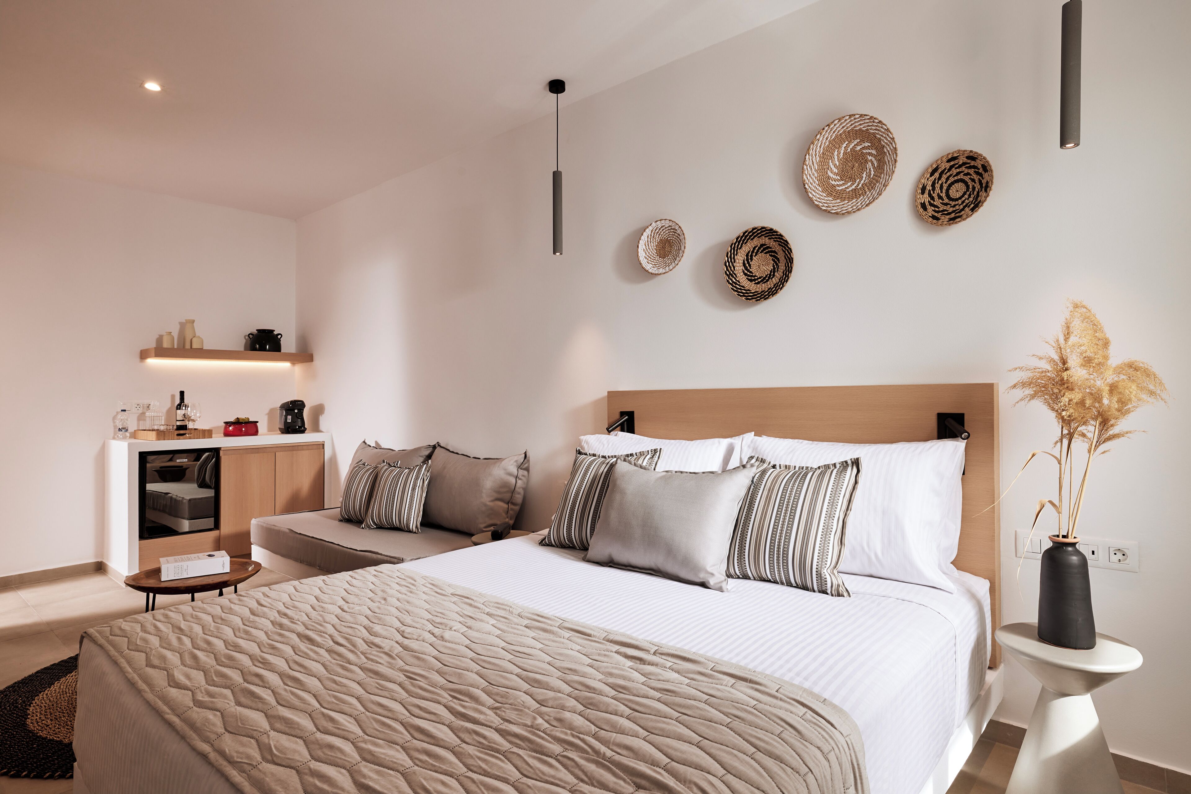 A modern bedroom with a large bed, bedside tables, a small desk, and a wall-mounted shelf with decorative items.