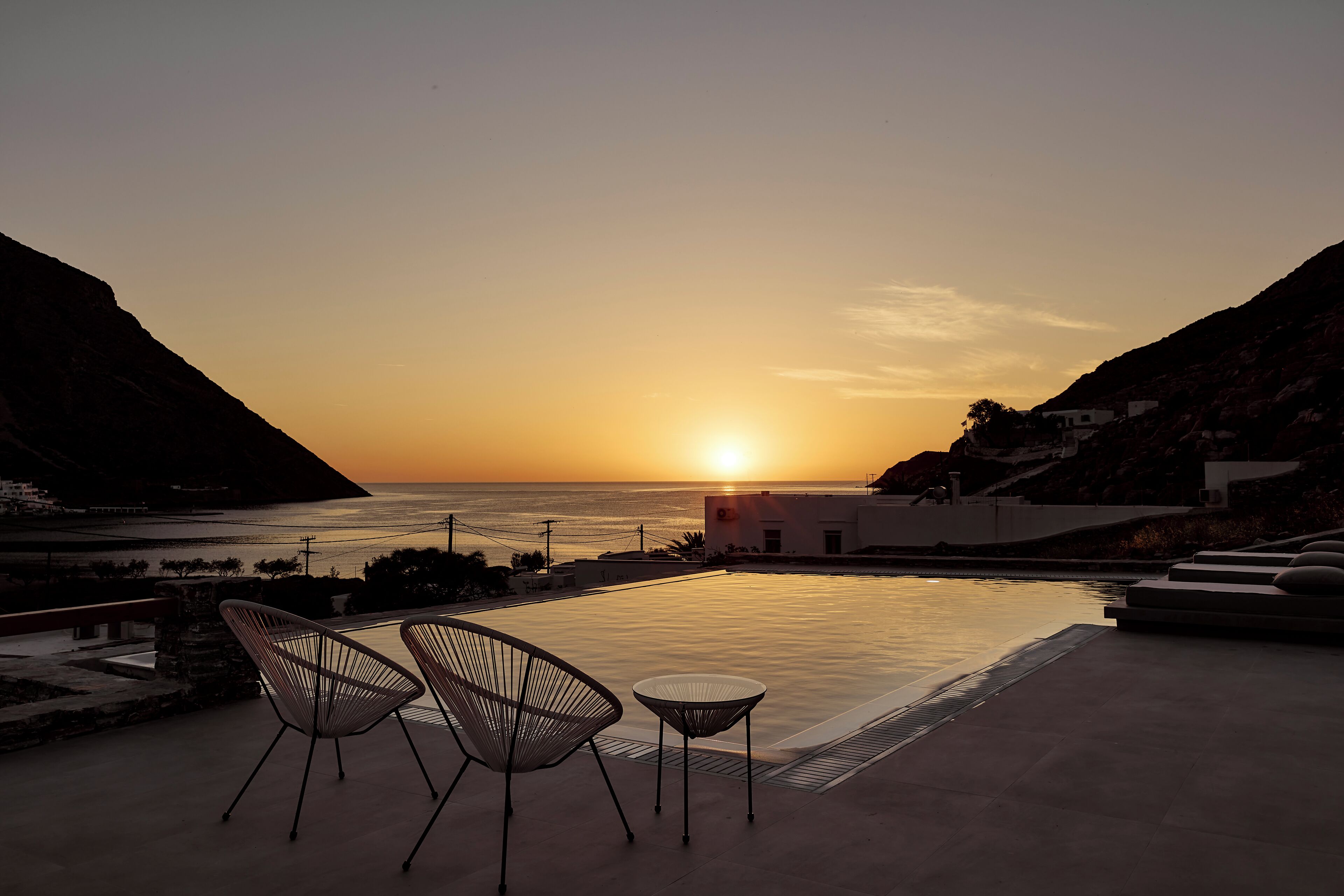 A sunset view from a terrace with a pool, two chairs, and a small table.