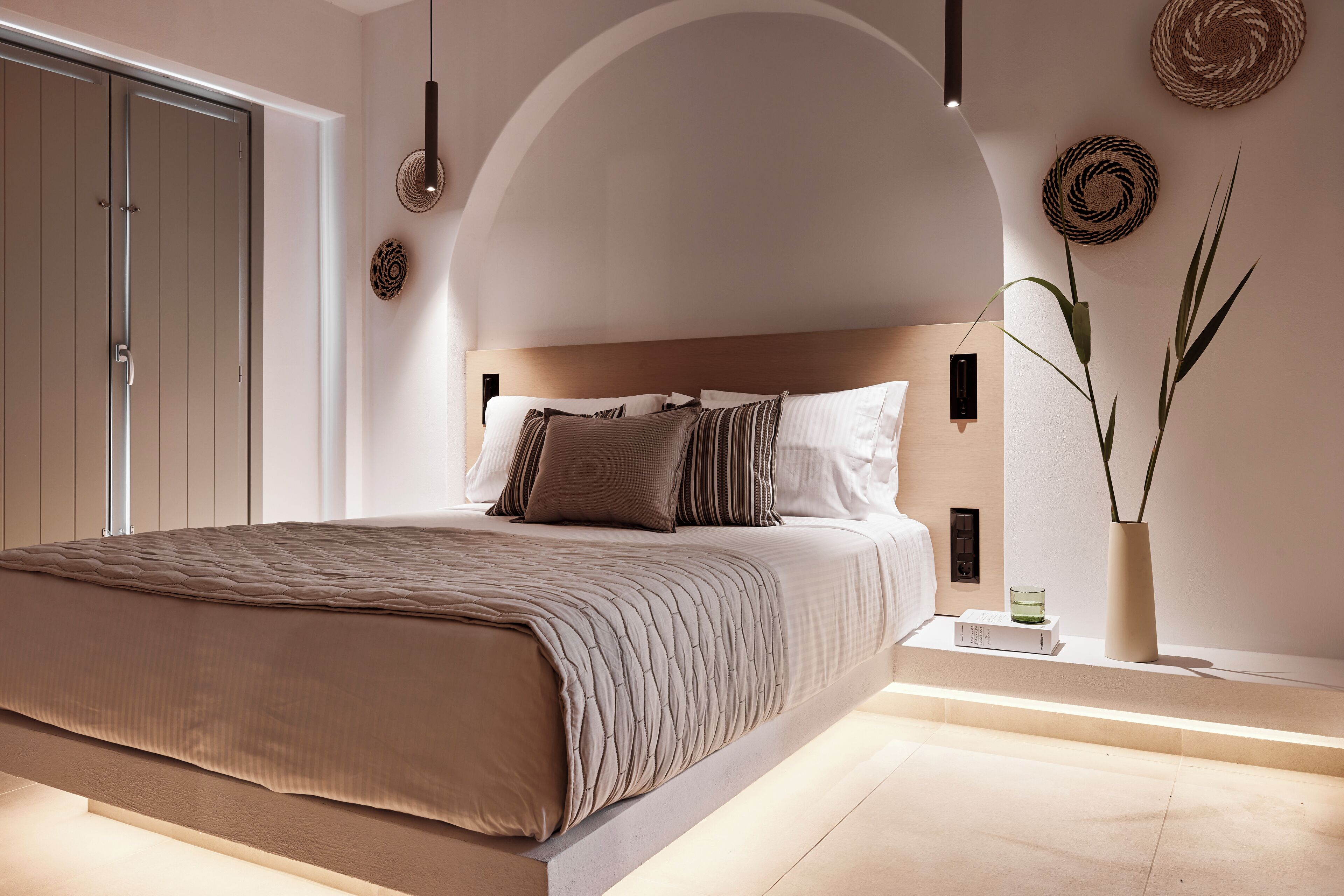 A modern bedroom with a large bed, a wooden headboard, and a bedside table with a book and a vase.