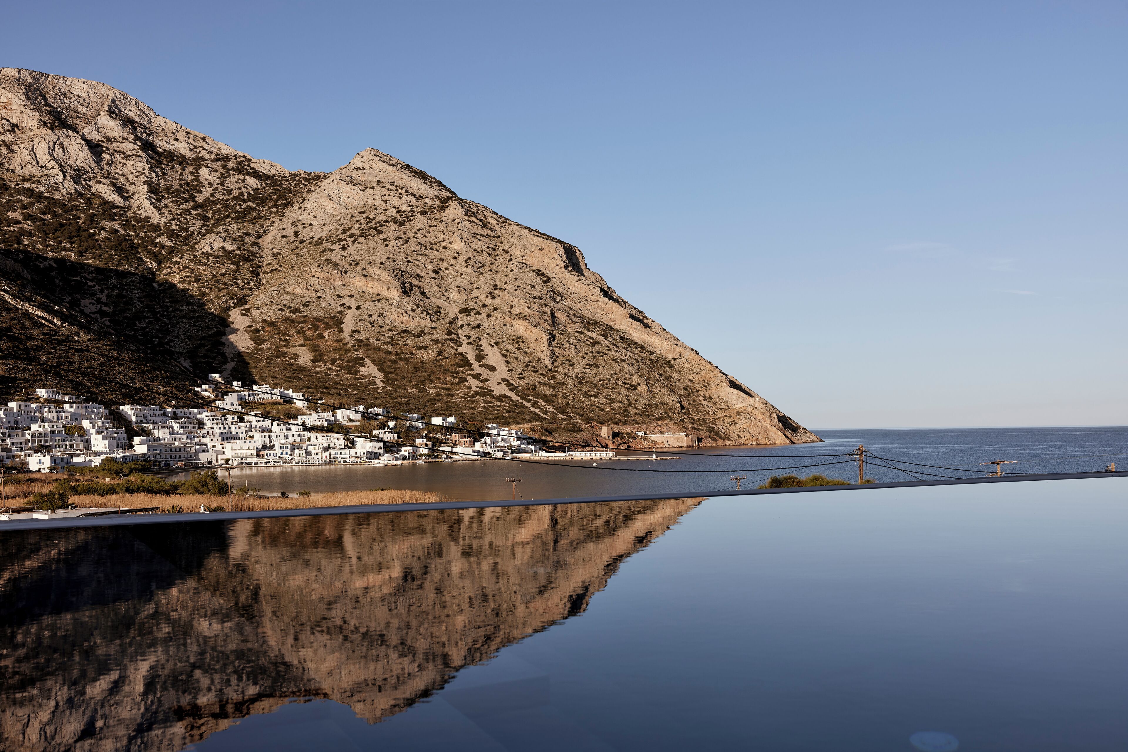 A coastal town with white buildings, a calm sea, and a mountain in the background.