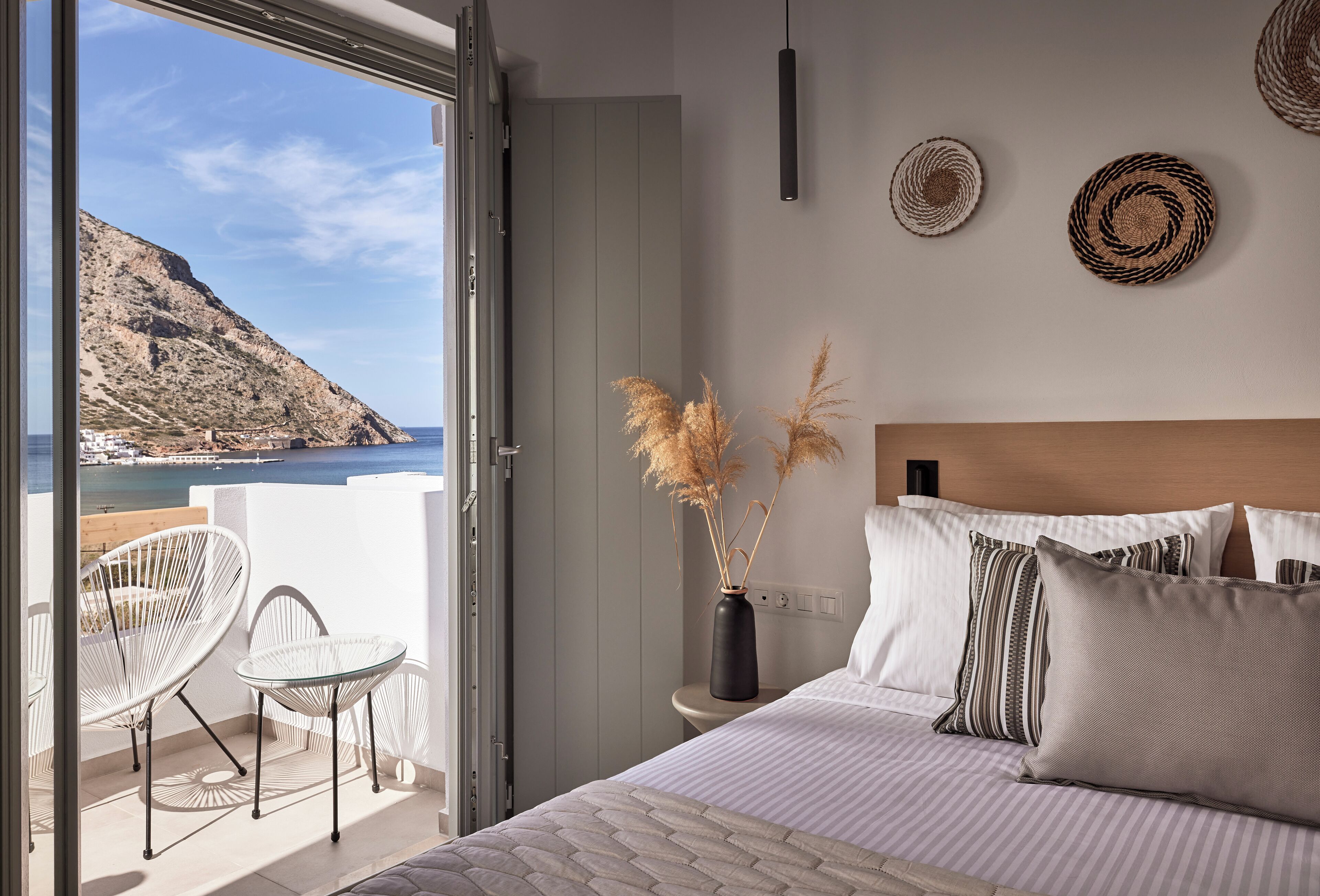 A bedroom with a large bed, a view of the sea, a balcony with chairs, and decorative wall art.