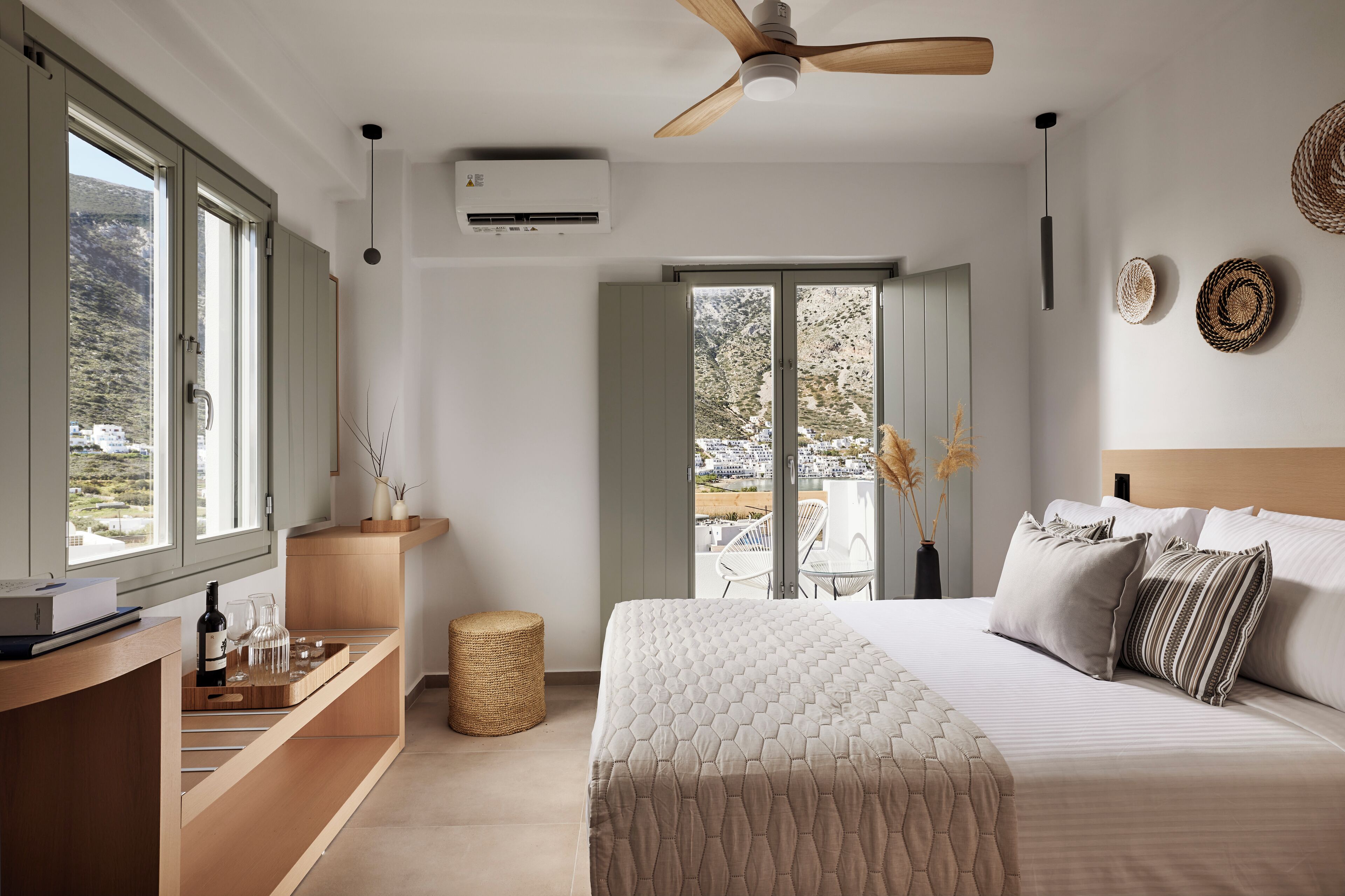 Un dormitorio moderno con una cama grande, un escritorio de madera, un ventilador de techo y vistas al exterior a través de una puerta corrediza.