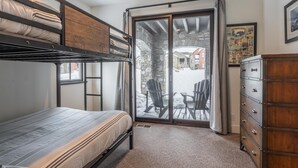 Une chambre avec un lit superposé, une commode en bois et une porte-fenêtre coulissante donnant sur un espace extérieur enneigé.