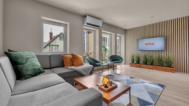 Ein modernes Wohnzimmer mit einem grauen Sofa, einem Holztisch und einem Fernseher, der 'NETFLIX' zeigt.