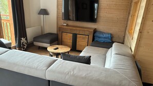 Una sala de estar moderna con un amplio sofá seccional en forma de L, una mesita redonda pequeña y un televisor montado en una pared de madera.