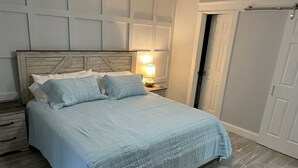 Une chambre avec une tête de lit en bois, un lit recouvert d’une couvre-lit bleu clair, une lampe de chevet et une porte sur le côté droit.