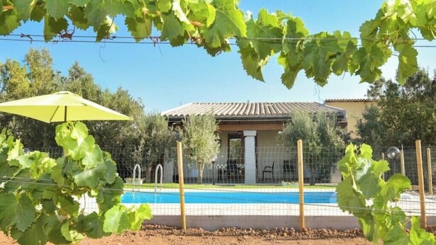 A pool area with a house in the background, surrounded by a fence and greenery. - Villetta Saeprus (Muravera)