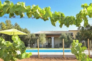 A pool area with a house in the background, surrounded by a fence and greenery. - Villetta Saeprus (Muravera)