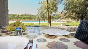 A table set outdoors with plates, cutlery, and a bottle of water, overlooking a pool and greenery. - Villetta Saeprus (Muravera)
