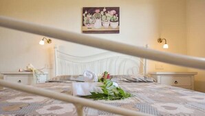 A neatly made bed with a patterned bedspread, a white headboard, and a painting of cacti on the wall. - Villetta Saeprus (Muravera)