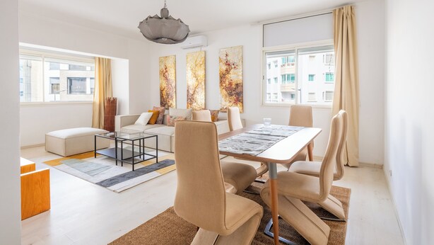 A modern living room with a dining area, large windows, and a view of buildings outside. - Charming apartment, in the heart of Agdal, 2 rooms (Rabat)