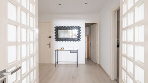 A hallway with a modern mirror, a small table with a bowl and a glass, and a wooden door at the end. - Charming apartment, in the heart of Agdal, 2 rooms (Rabat)