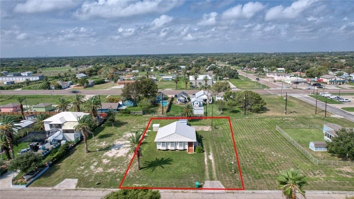A residential area with a house surrounded by a fenced yard, a road, and other houses in the background.