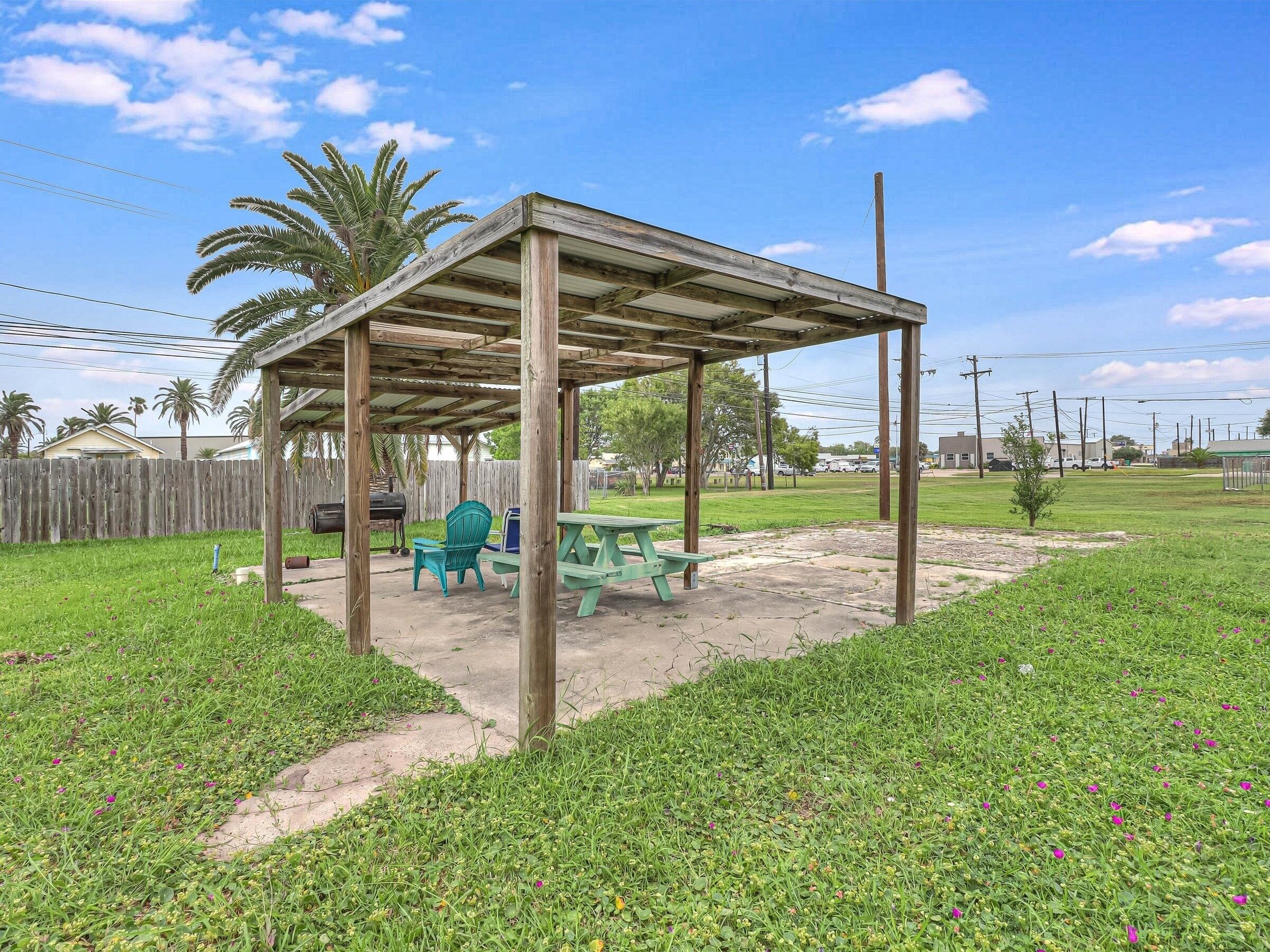 A wooden pergola with a picnic table and chairs in a grassy backyard.