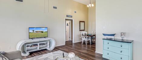 A living room with a TV, a ceiling fan, a dining area with a table and chairs, and a light blue dresser.