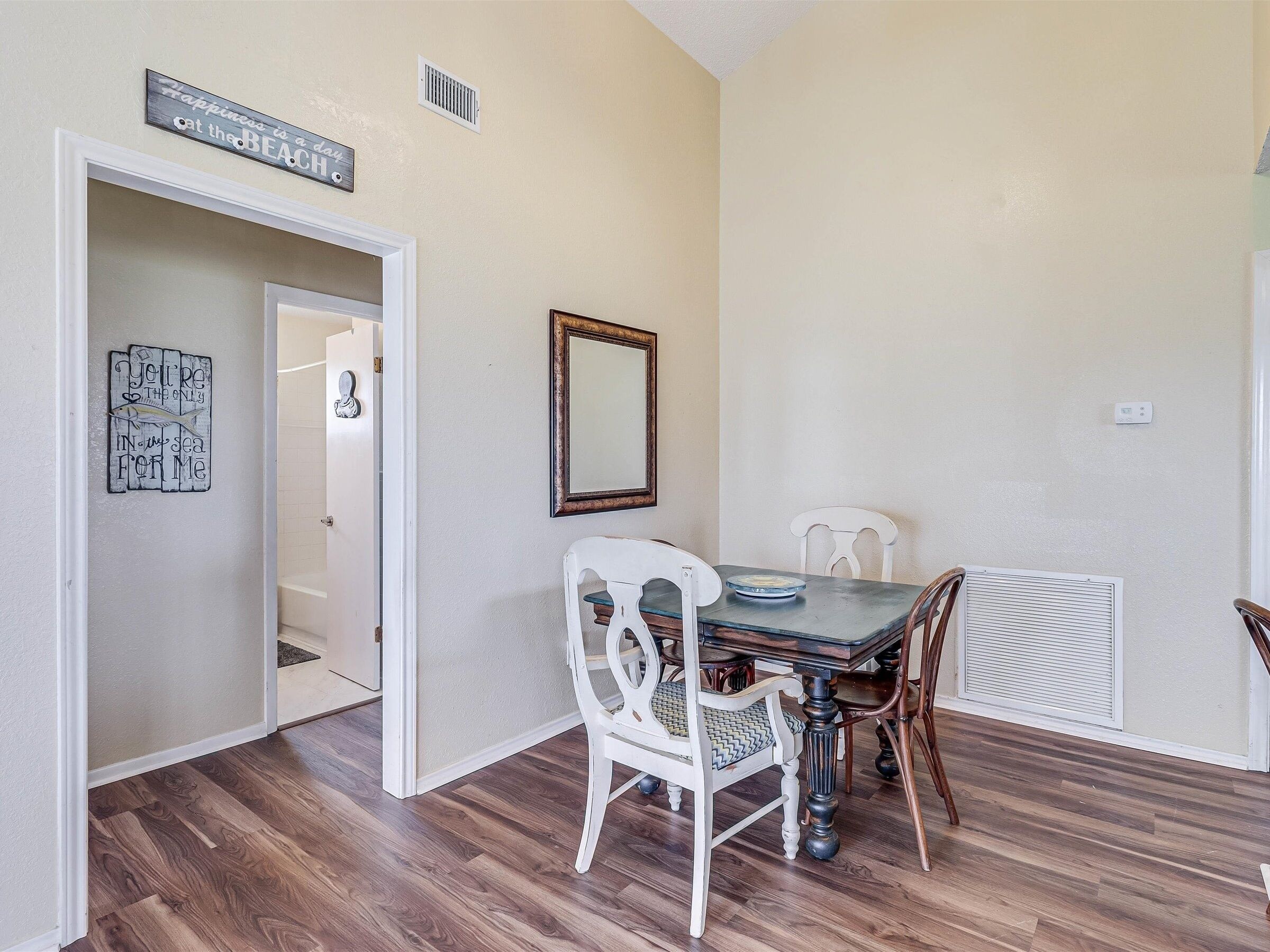 A dining area with a table and chairs, a mirror, and a sign on the wall.