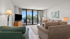 Una sala de estar con sofá, televisor y balcón con vista a palmeras.
