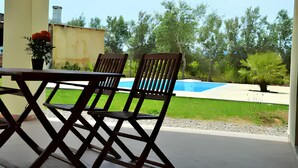 A patio with a table and two chairs, a swimming pool, and surrounding greenery. - An oasis of tranquility near the beautiful beaches of Sarrabus. (Muravera)