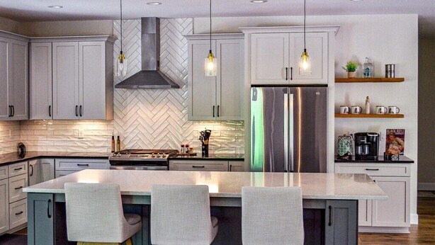 Une cuisine moderne avec des armoires blanches, un réfrigérateur en acier inoxydable et un dosseret décoré d’un motif en chevrons.
