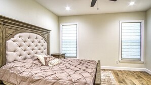 Une chambre à coucher avec une tête de lit capitonnée, un grand lit recouvert d’une courtepointe rose, deux tables de chevet et un plancher en bois.
