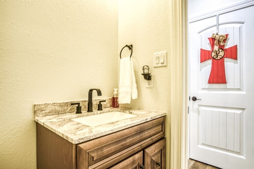 Un baño con lavamanos de mármol, tocador de madera y una puerta blanca con un adorno rojo.