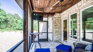 Un espace extérieur abrité, doté d’un mur en briques, de grandes fenêtres et d’une table avec des coussins bleus.