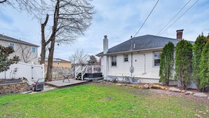 A residential backyard with a lawn, a wooden deck, a house, and a chimney. - Welcoming Glen Cove Home ~ 1 Mi to Public Beach! (Glen Cove)