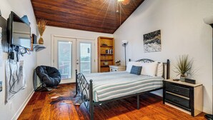 Un dormitorio con suelo de madera, una cama, un escritorio, una silla, una estantería y un cuadro en la pared.