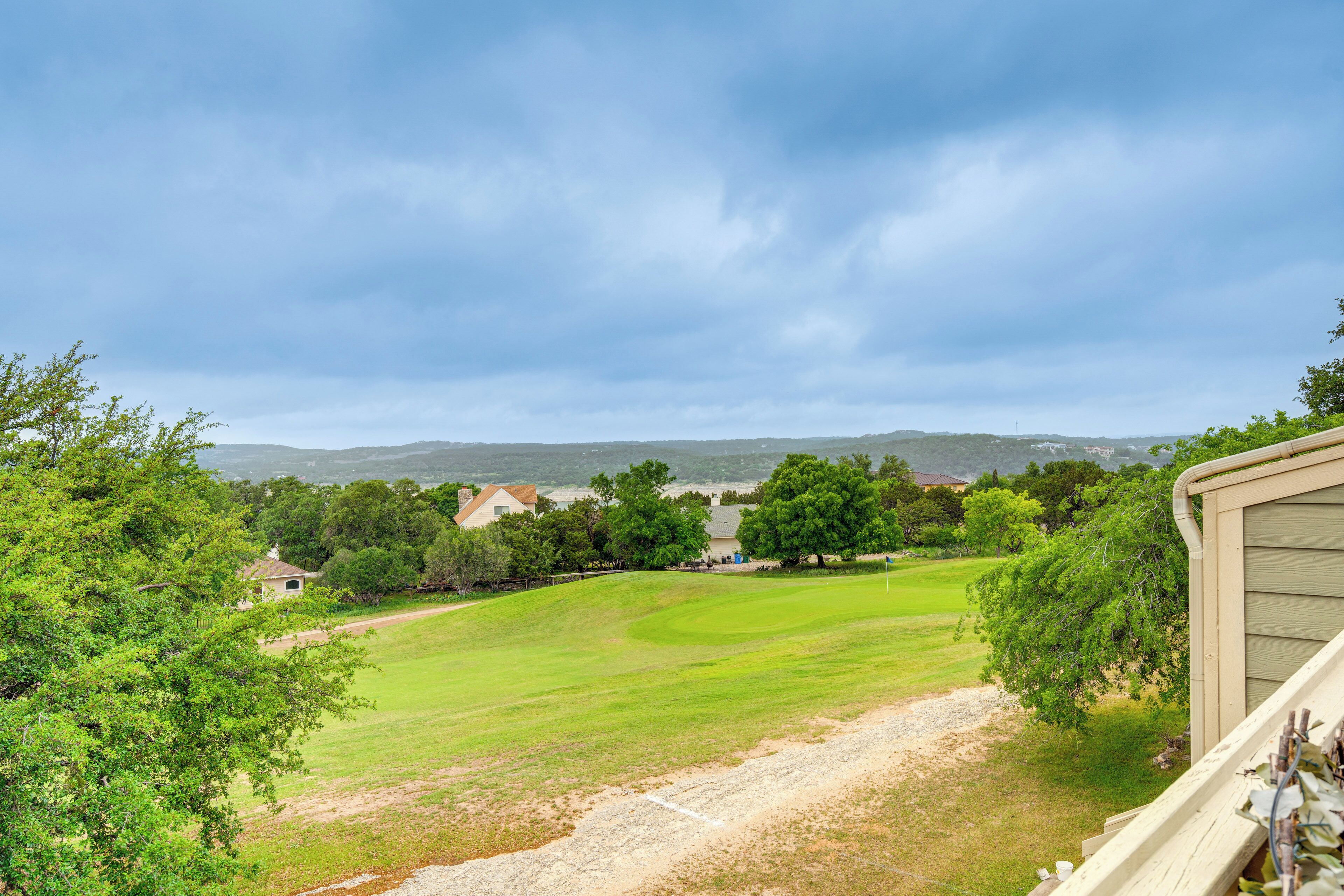 A view of a green field with a house in the background and a cloudy sky.