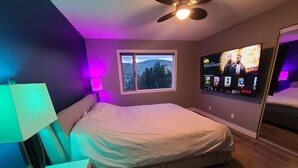 A bedroom with a bed, a window, a TV mounted on the wall, and a ceiling fan.
