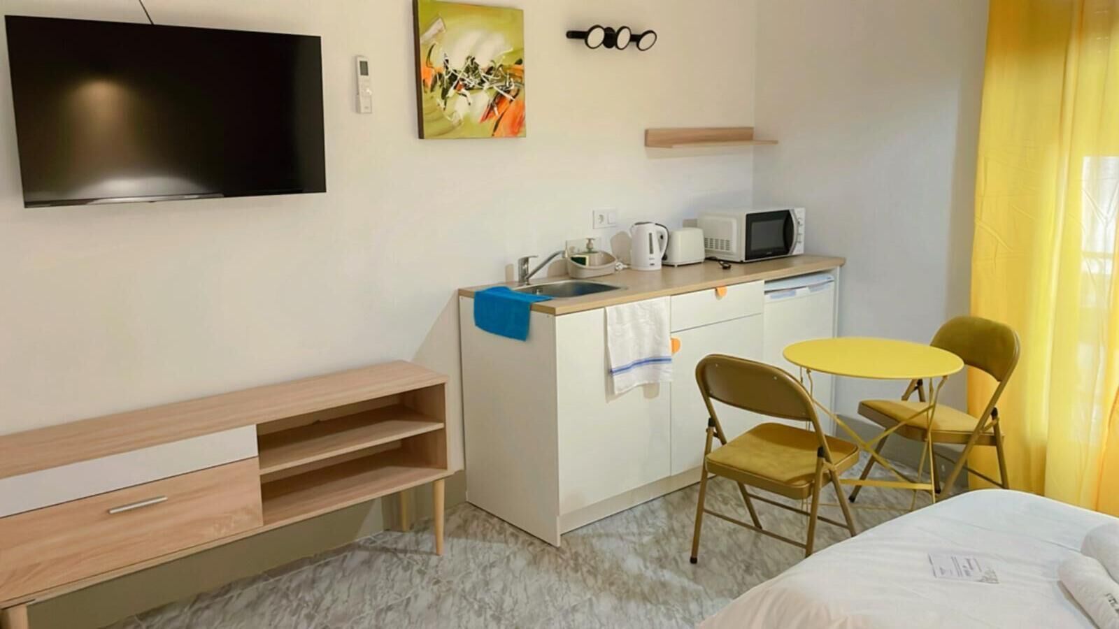 Une chambre d’hôtel comprenant un lit, un bureau avec un ordinateur, un four à micro-ondes, une bouilloire et une petite table avec deux chaises.