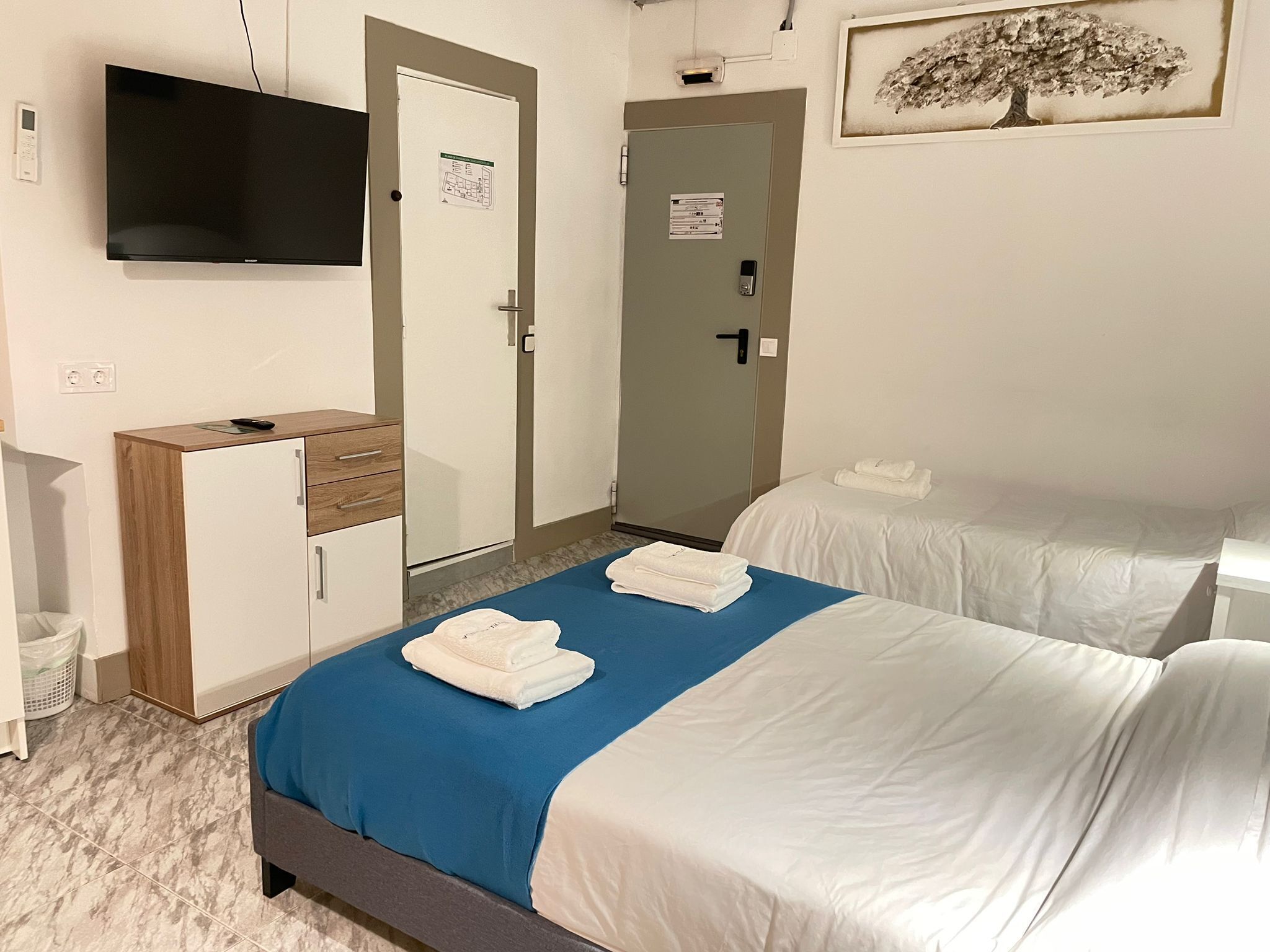 A hotel room with two beds, a desk, a television, and a door with a map.