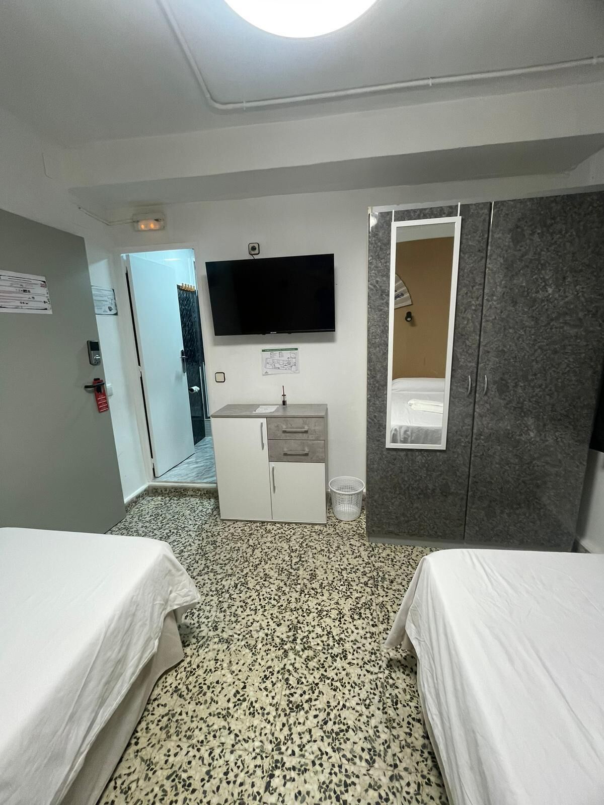 A hotel room with two beds, a TV, a wardrobe, and a small desk.
