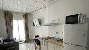 A compact kitchen with a microwave, sink, and a small refrigerator. There is a dining area with a chair and a sofa. - HOTEL ARGANDA (Arganda del Rey)
