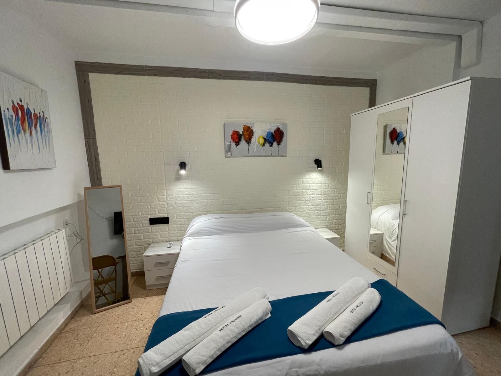 A hotel room with a large bed, a bedside table, a mirror, and a wardrobe.