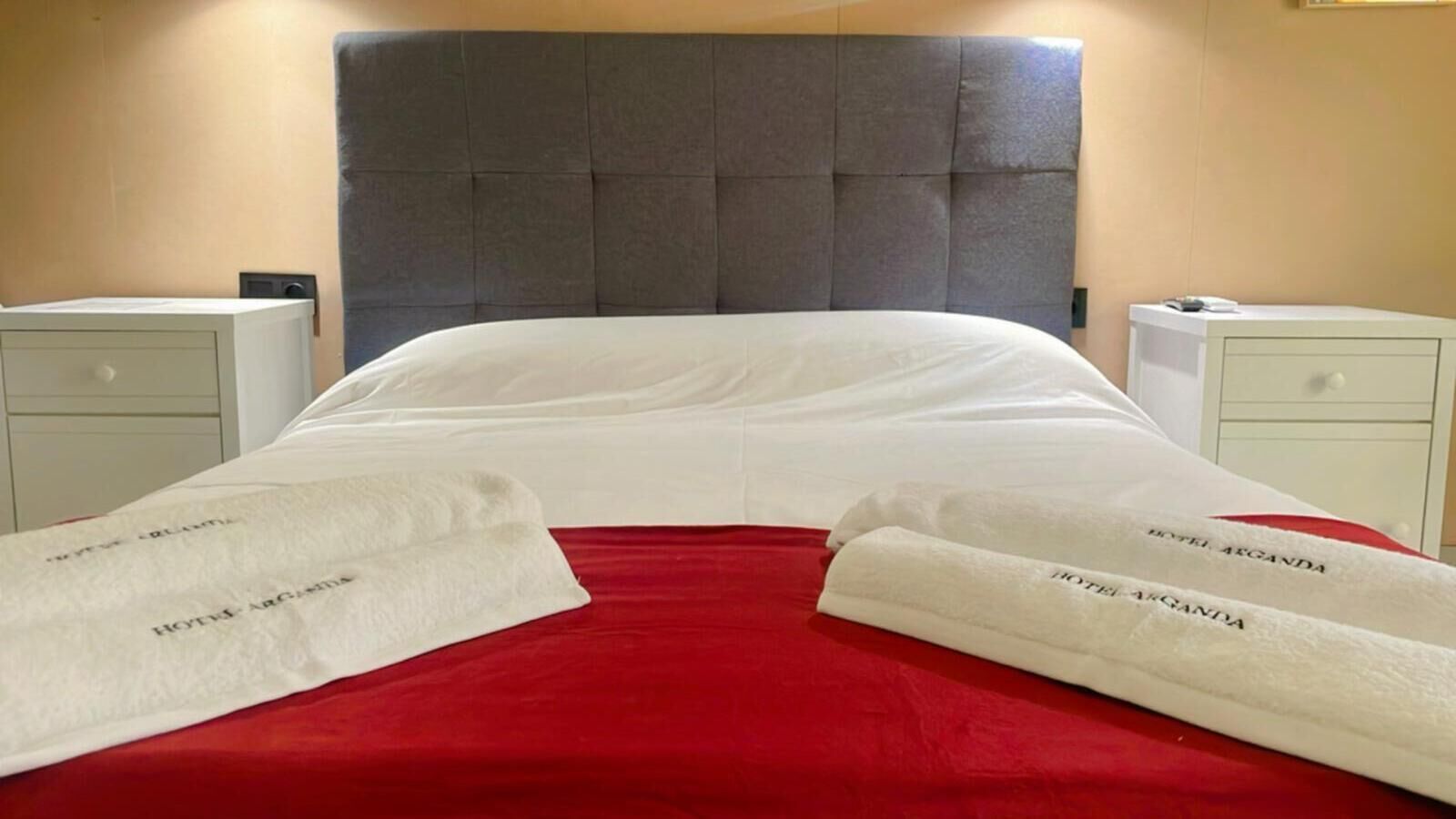 A hotel room with a large bed, two bedside tables, and a red bedspread.