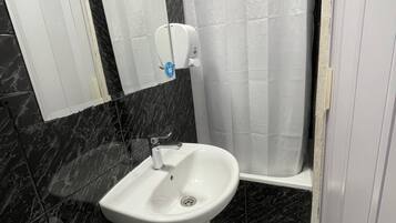 Un bagno con un lavandino bianco su piedistallo, uno specchio, un dispenser per asciugamani, un porta carta igienica e una tenda da doccia.