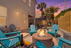 Un patio al aire libre con sillas Adirondack turquesa, un pozo de fuego redondo y una mesa de comedor.