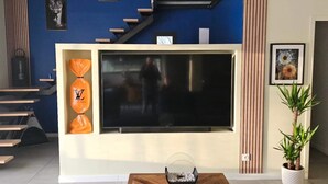 En moderne stue med et stort fladskærms-tv på væggen, et træsofabord i midten og en trappe, der fører op til et højere niveau.