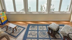 Ein Zimmer mit großem Fenster mit Blick auf ein Gewässer, einem kleinen Tisch, einem gemusterten Teppich und einem Stuhl.