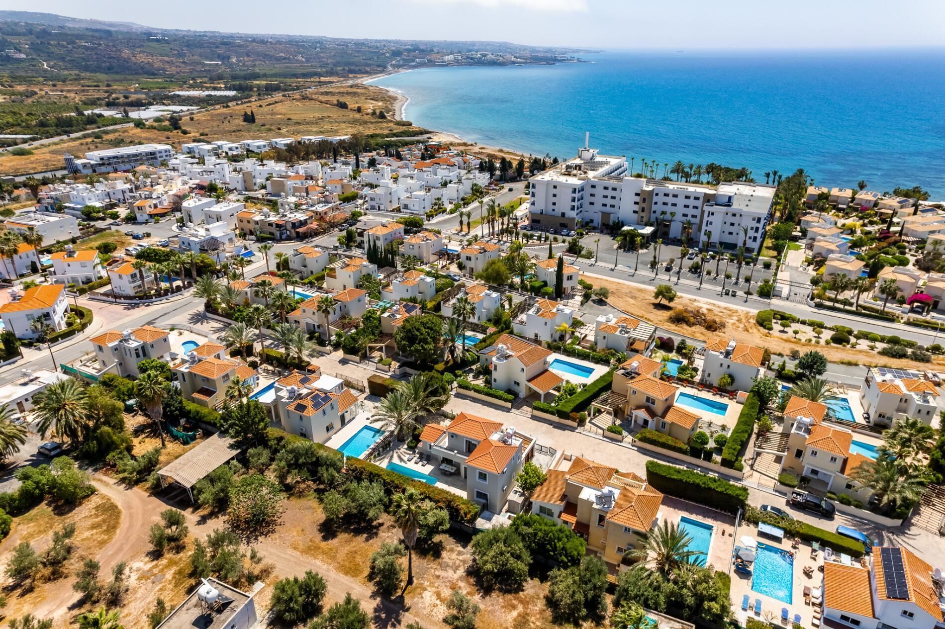 Vista aérea de una zona residencial costera con edificios blancos, algunos con tejados de tejas rojas, y una vista despejada del mar.