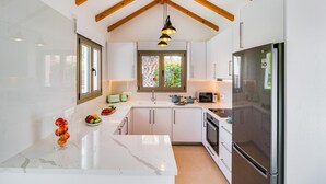 A modern kitchen with white cabinets, a marble countertop, a stainless steel refrigerator, and a wooden ceiling. - Villa Sophia by Ezoria Villas (Paphos)
