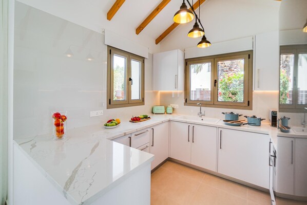 A modern kitchen with white cabinets, a marble countertop, and wooden beams on the ceiling.